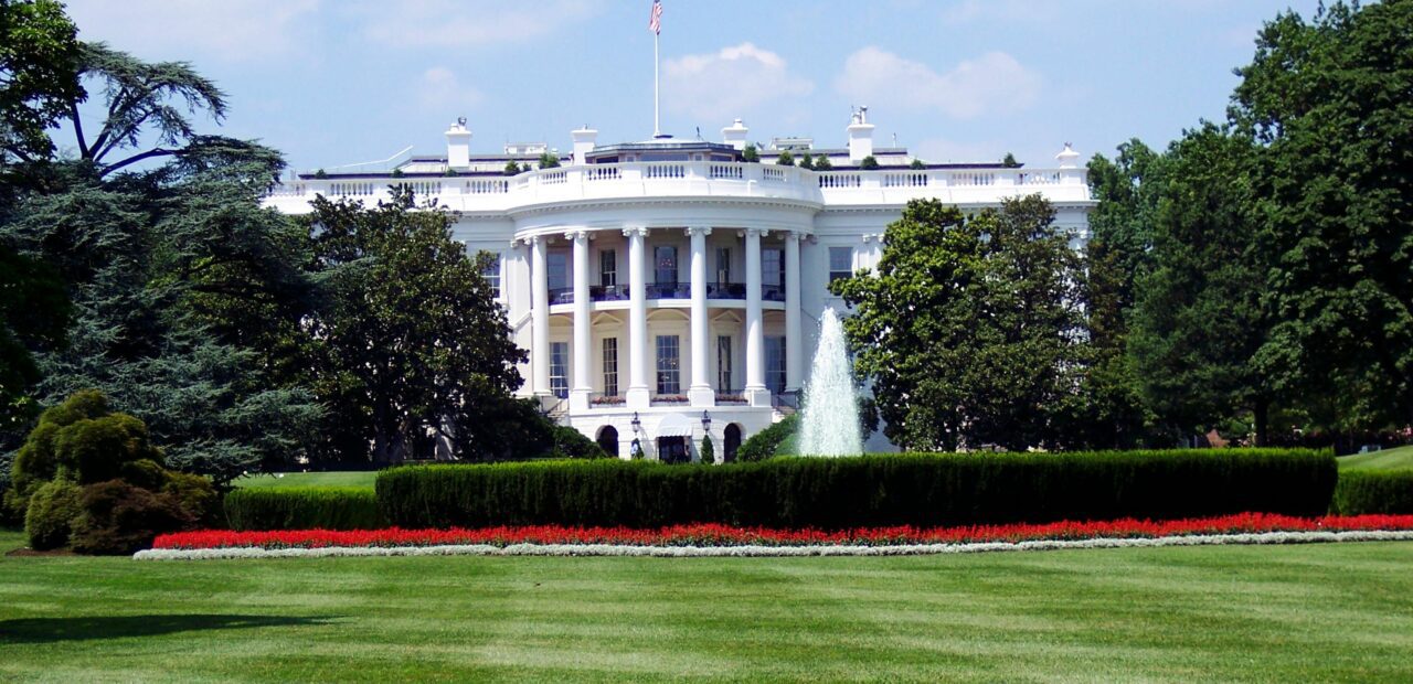 Iconic view of the White House with lush gardens and a central fountain on a sunny day.