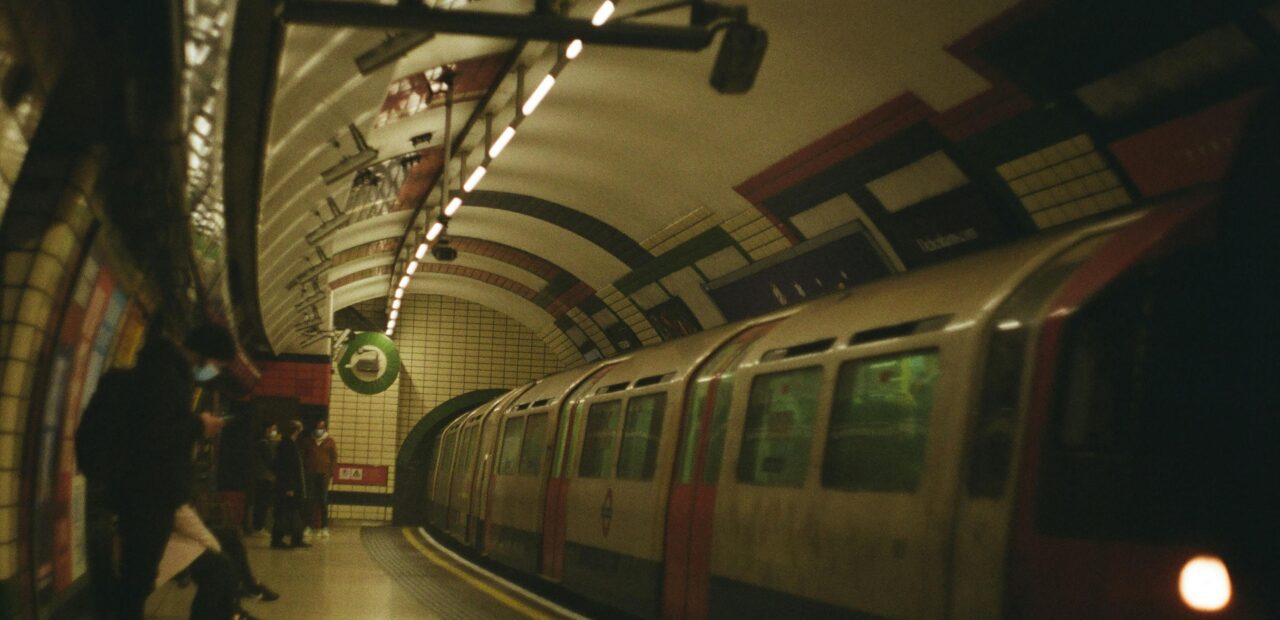 A subway train arrives at an underground station in London, UK, with commuters waiting on the platform.