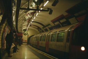 A subway train arrives at an underground station in London, UK, with commuters waiting on the platform.